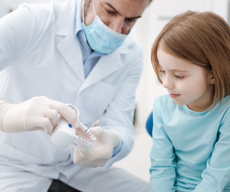 Dentist showing a dental model to a young child before a tooth filling procedure, illustrating safe dental care for toddlers.